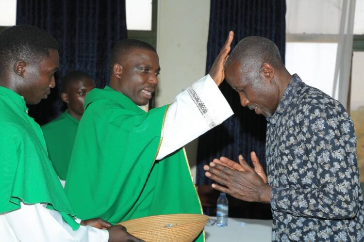 Rev. Fr. Kiibi while blessing the Dean School of Commercial Industrial Art and Design, Mr. Charles Kagwa Lwanga.