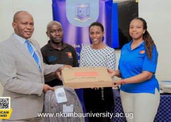Prof. Jude Lubega (in suit) and Ms. Kayla Tetsi Lubega (In Blue T-shirt) handing over a laptop to one of the Scholars