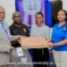 Prof. Jude Lubega (in suit) and Ms. Kayla Tetsi Lubega (In Blue T-shirt) handing over a laptop to one of the Scholars